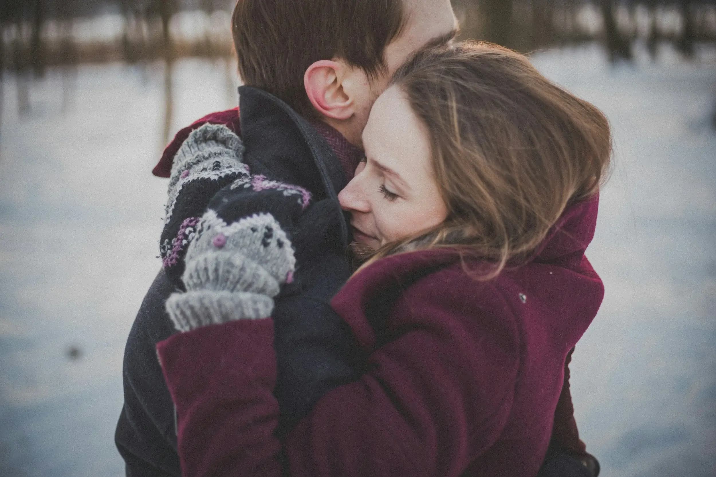A couple holding each other close outdoors in winter light.